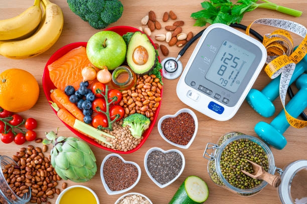 Heart-shaped bowl of salmon, fruit and vegetables beside a blood pressure monitor, nuts, seeds and dumbbells
