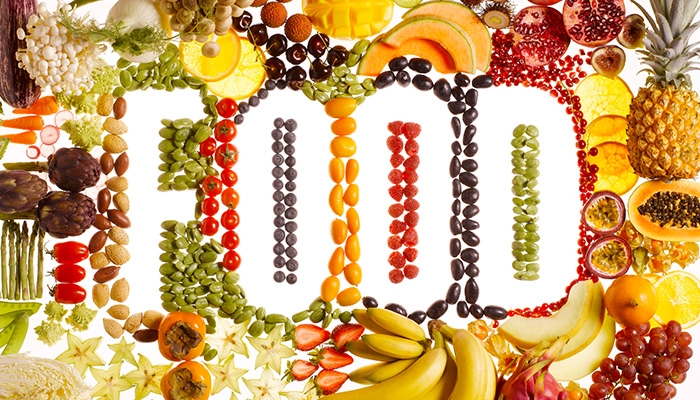 The word FOOD spelled out with seeds and beans, framed by assorted fresh fruits and vegetables on white