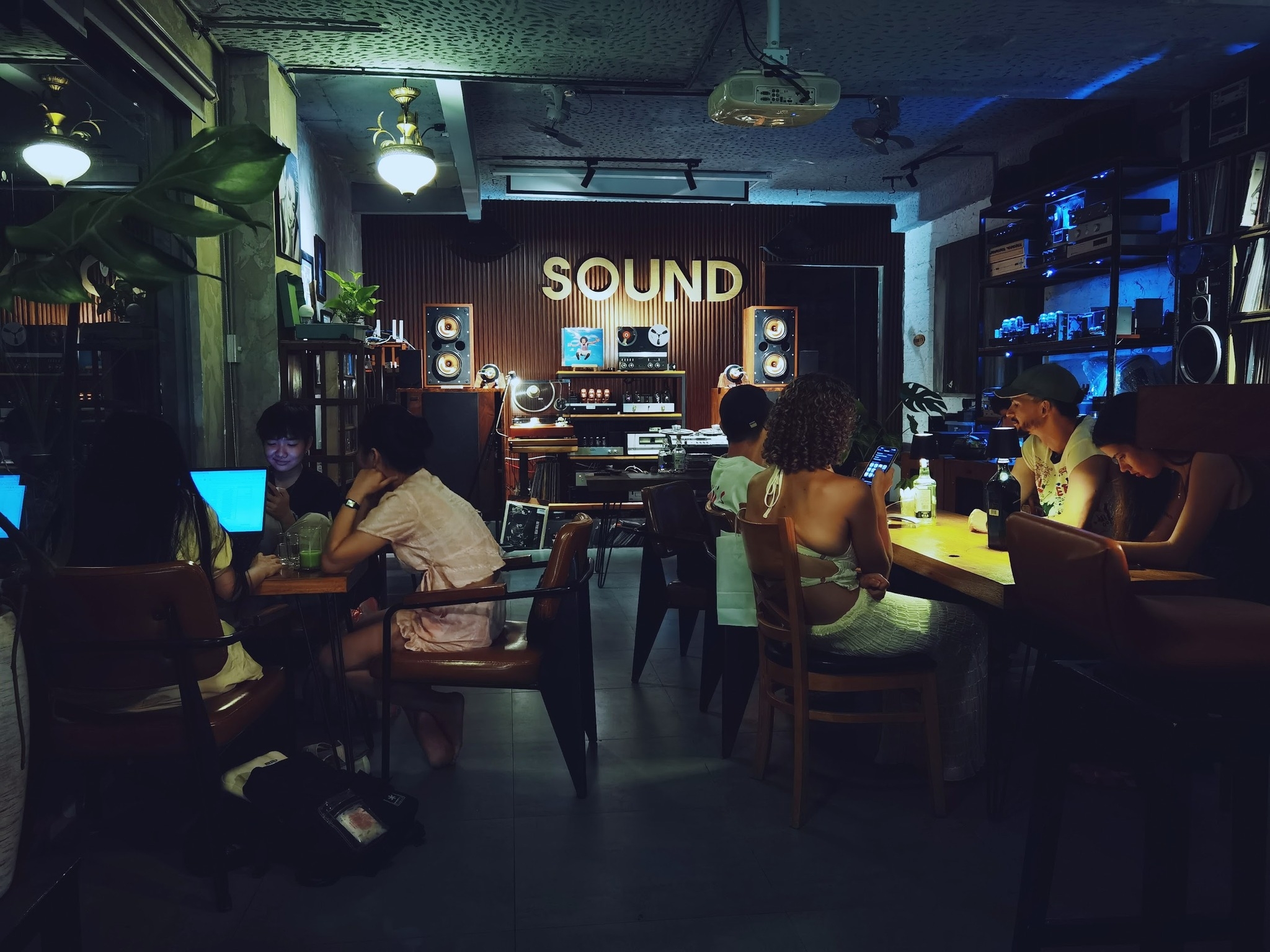 Dim vintage cafe interior with a Sound sign, hi-fi speakers and turntable, and people relaxing at wooden tables