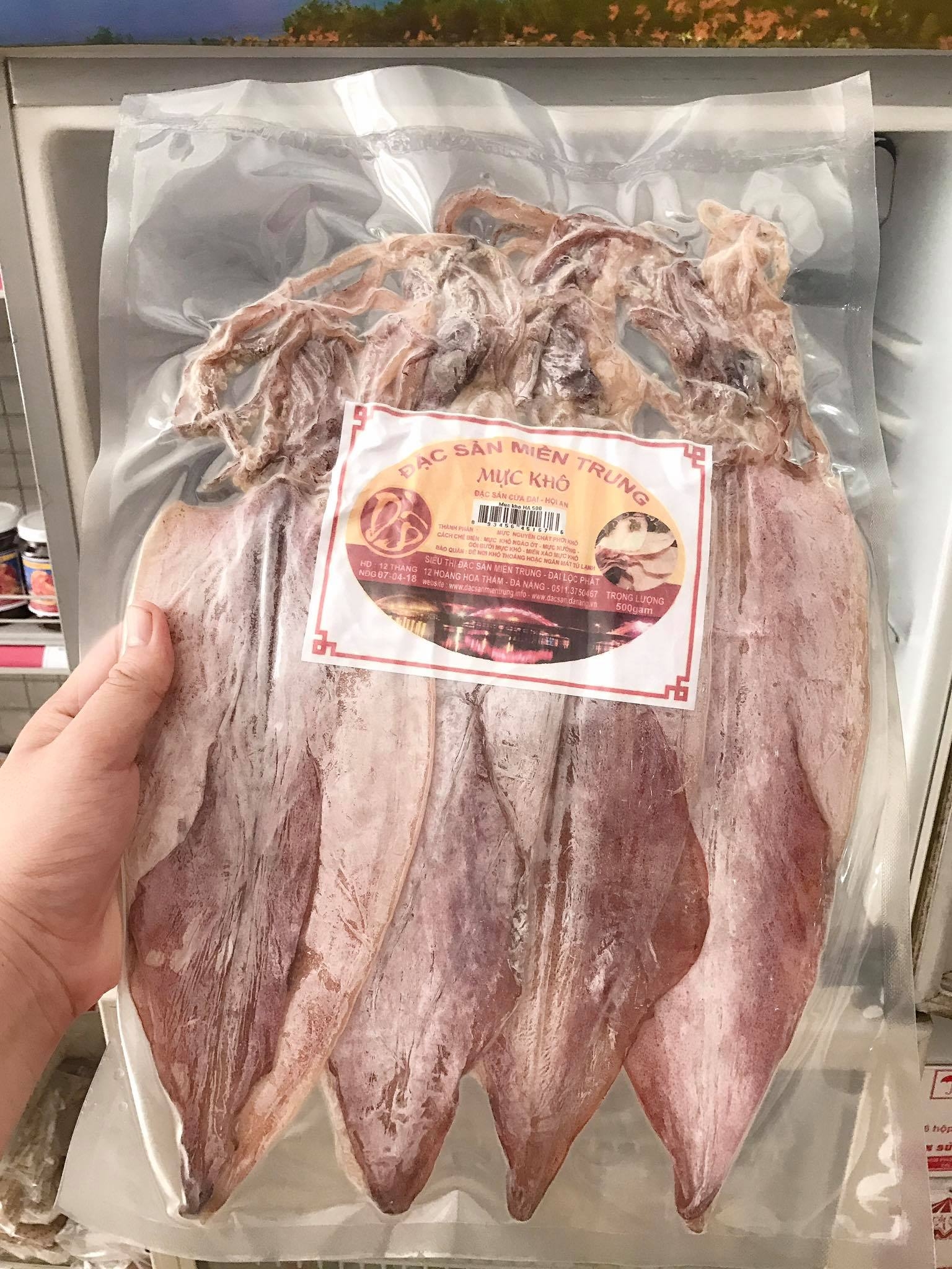 Hand holding a vacuum sealed pack of whole dried squid labeled as a Central Vietnam specialty