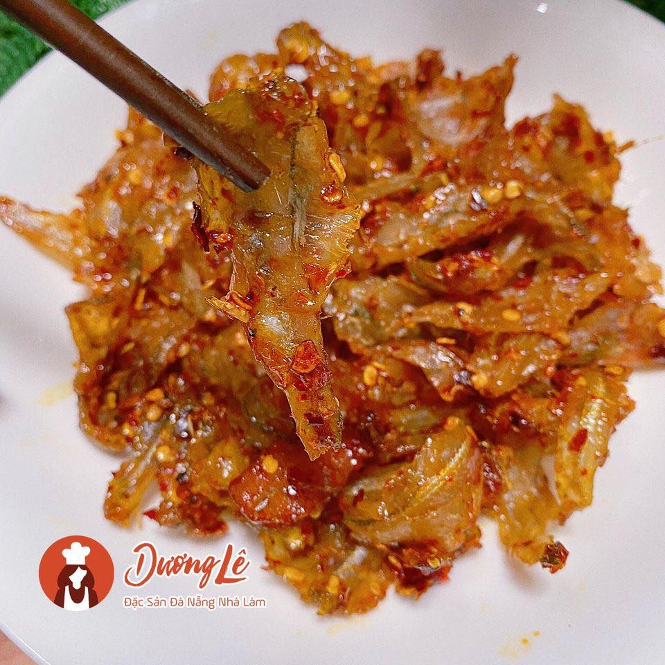 Plate of small dried fish coated in red chili sauce lifted with wooden chopsticks, with a Duong Le logo