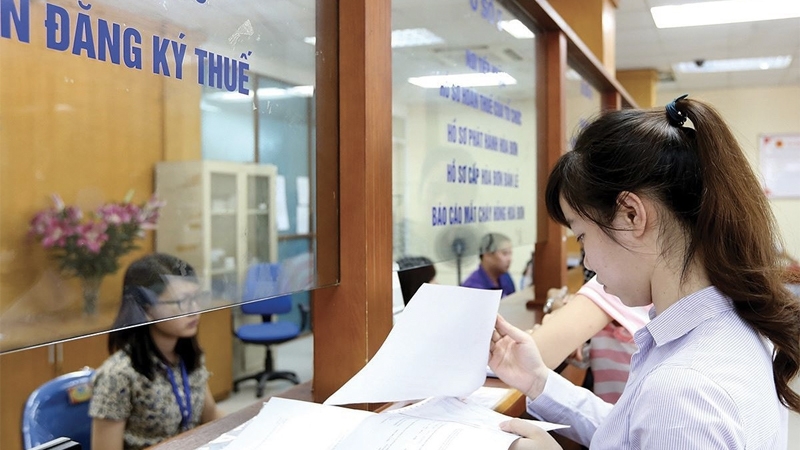 Woman holding documents at a Vietnamese tax registration office counter with a clerk behind the glass