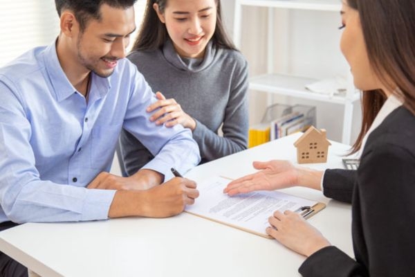 Young couple signing a rental agreement at a desk with an agent and a small house model nearby