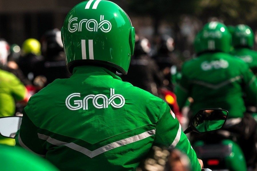 Grab motorbike drivers in green Grab jackets and helmets seen from behind while riding in city traffic