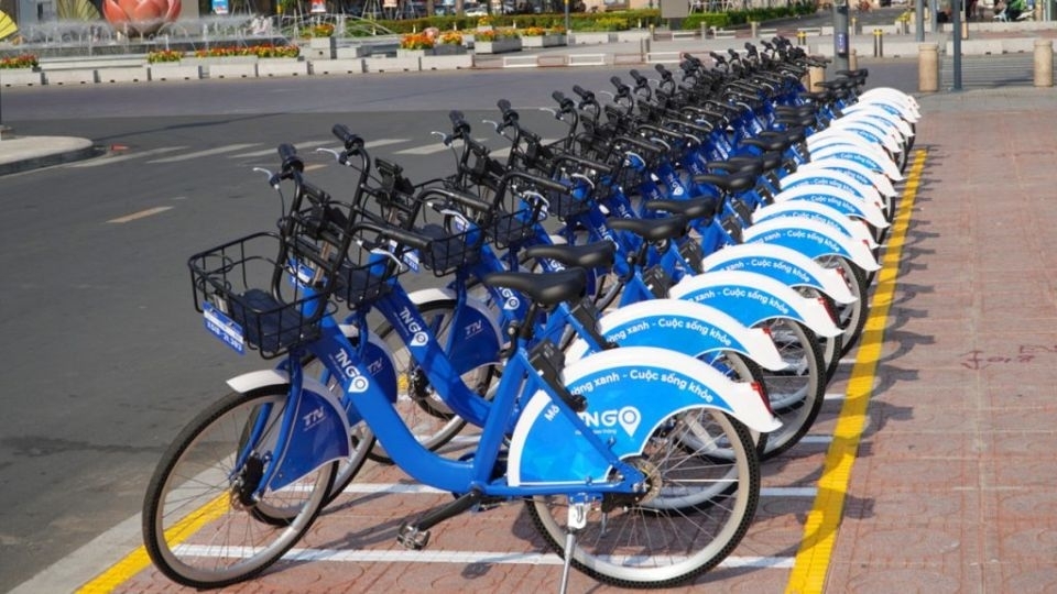 A long row of blue TNGo public rental bicycles parked at a station on a city street on a sunny day