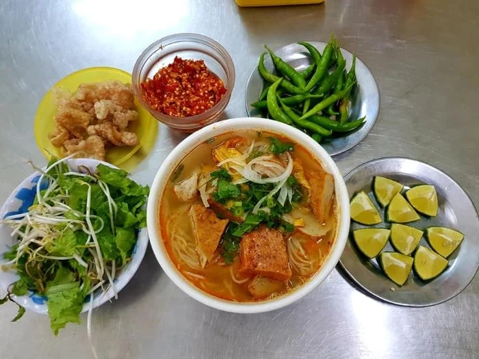 A side plate of fresh herbs, lime and sliced chili served with a Vietnamese noodle soup