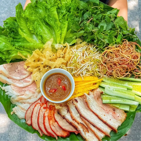 A Da Nang pork-and-herbs platter with sliced two-skin pork, lettuce, mint, perilla, green banana and cucumber arranged around soft rice paper