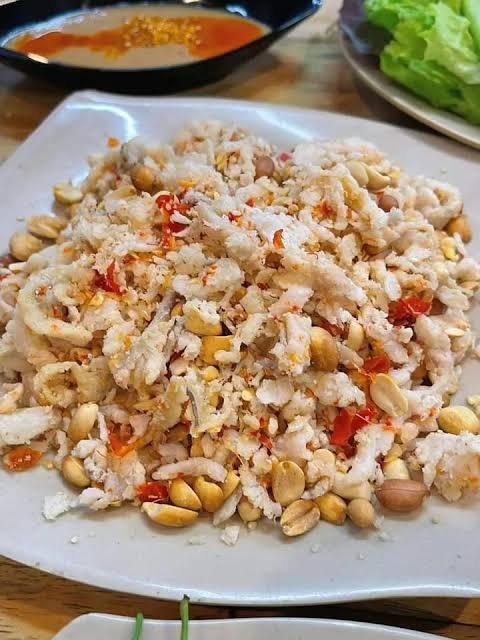 A dry-style plate of gỏi khô — cured fish dusted in toasted rice flour and peanuts, served with rice paper and herbs for wrapping