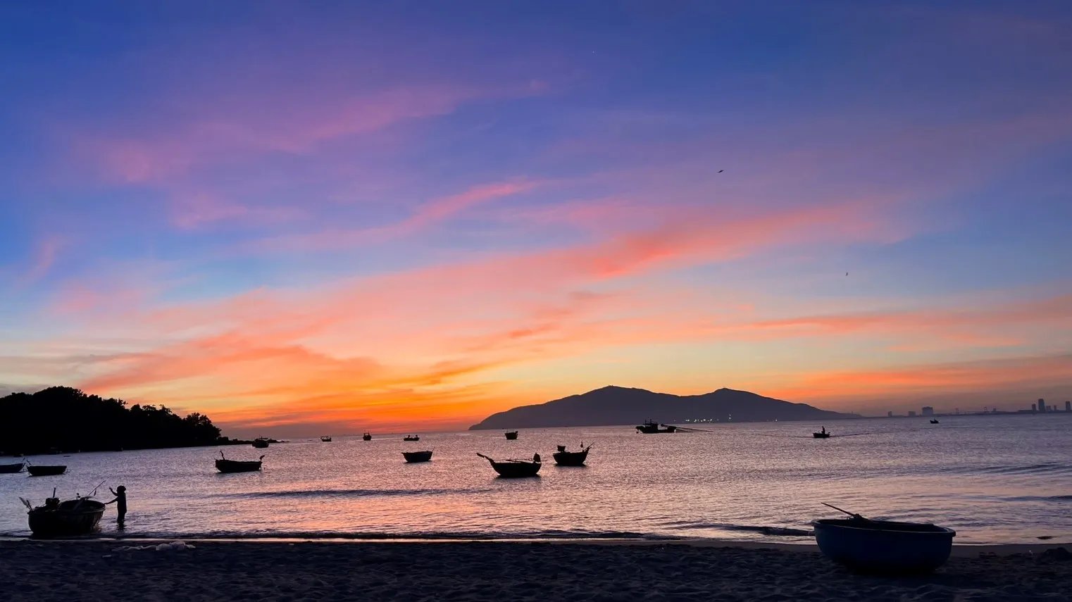 Fishing boats and round basket boats on the beach at a Da Nang fishing village at sunset — where the day's catch comes in fresh
