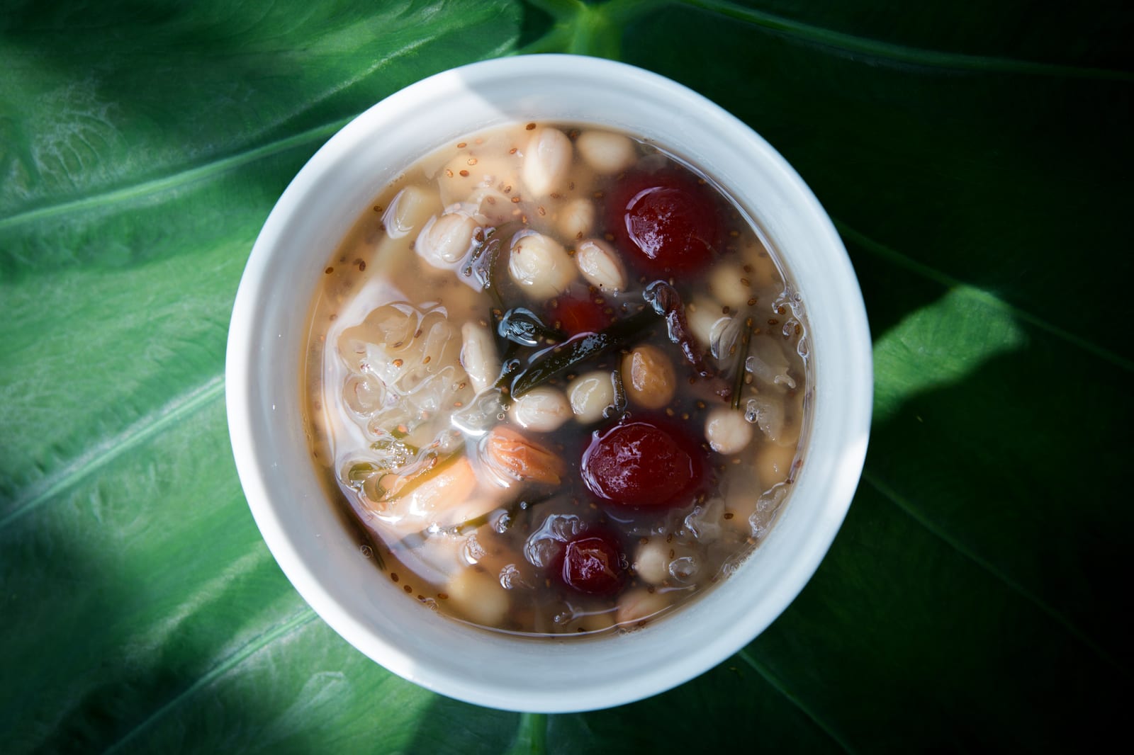 A bowl of chè thập cẩm with white beans, red jelly pearls, longan and lotus seeds in light syrup.
