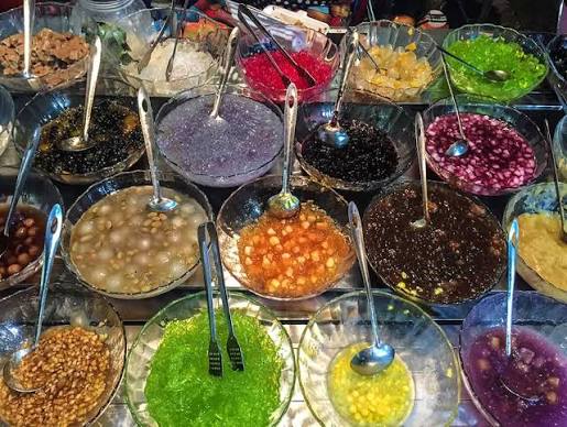 A Vietnamese street vendor's chè cart with jars of toppings and coconut milk.