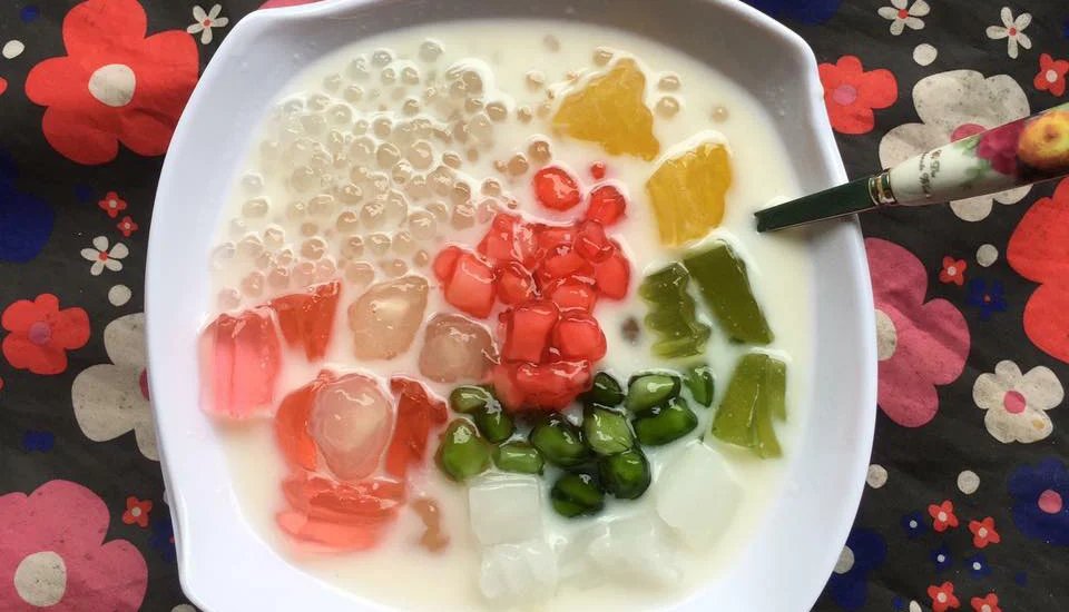 A long spoon stirring a glass of the mixed dessert with coconut milk.