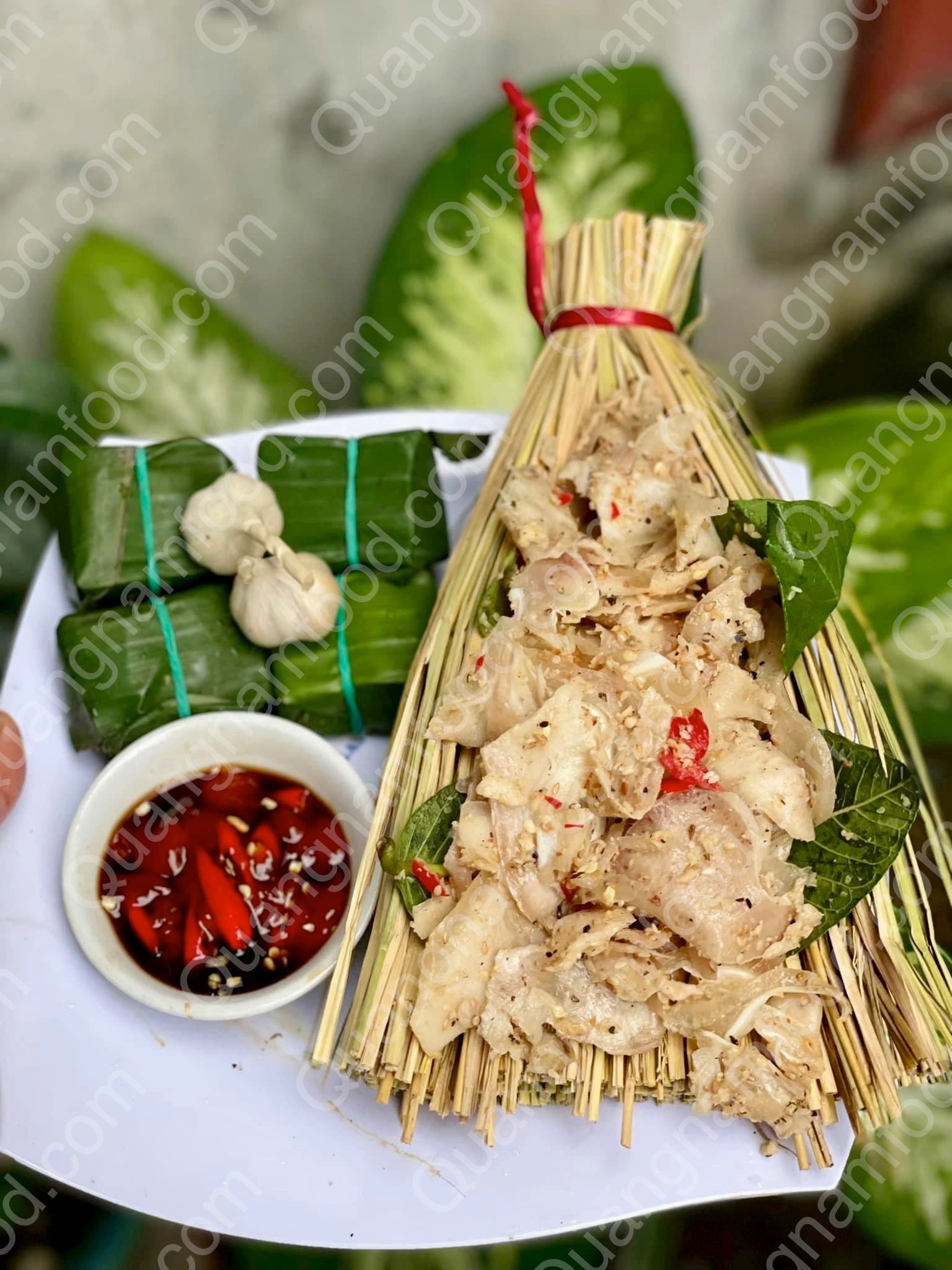 Bình Định tré bound in dried straw and tied broom-shaped — the regional tell, opened to show the shredded pork and served with a chili dip.