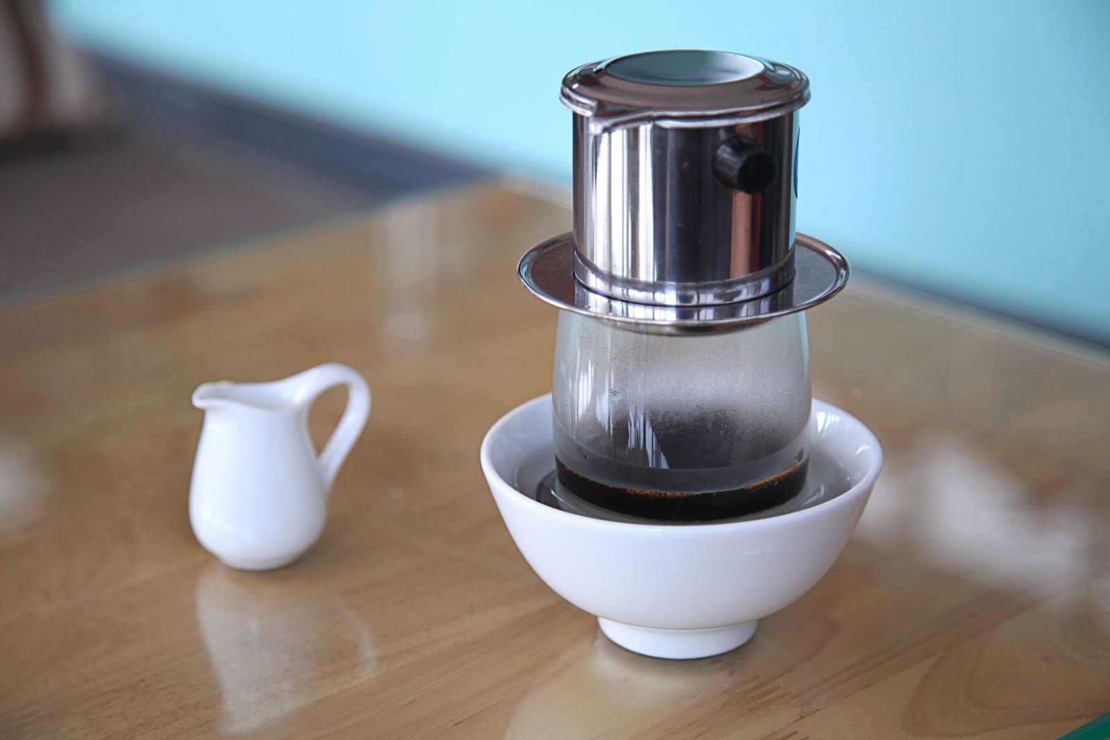 A metal Vietnamese phin filter slowly dripping dark coffee into a glass.