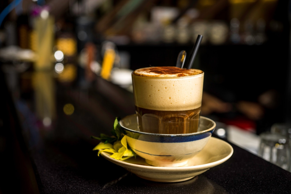A glass of Vietnamese egg coffee (cà phê trứng) topped with thick, fluffy whipped egg-yolk custard, served on a saucer.