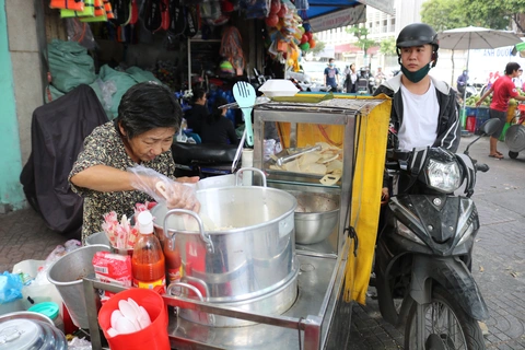 A street vendor serving breakfast from a roadside cart with steaming pots in Vietnam