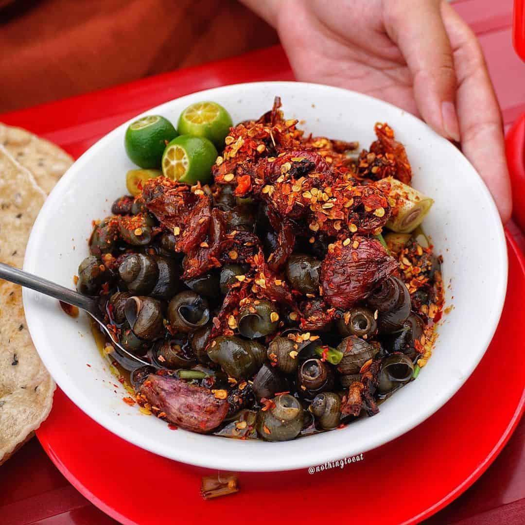 A diner slurping a small snail straight from its shell, the way ốc hút is eaten in Da Nang