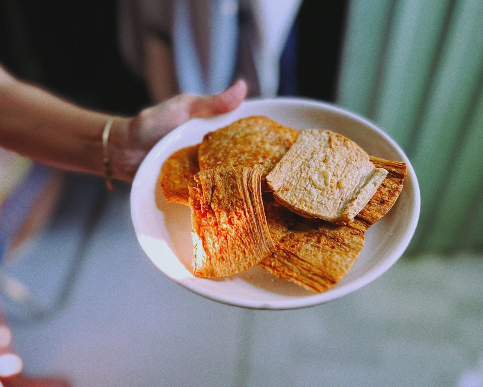 A toasted sesame rice cracker (bánh tráng mè) held over a bowl of mì Quảng, ready to crack