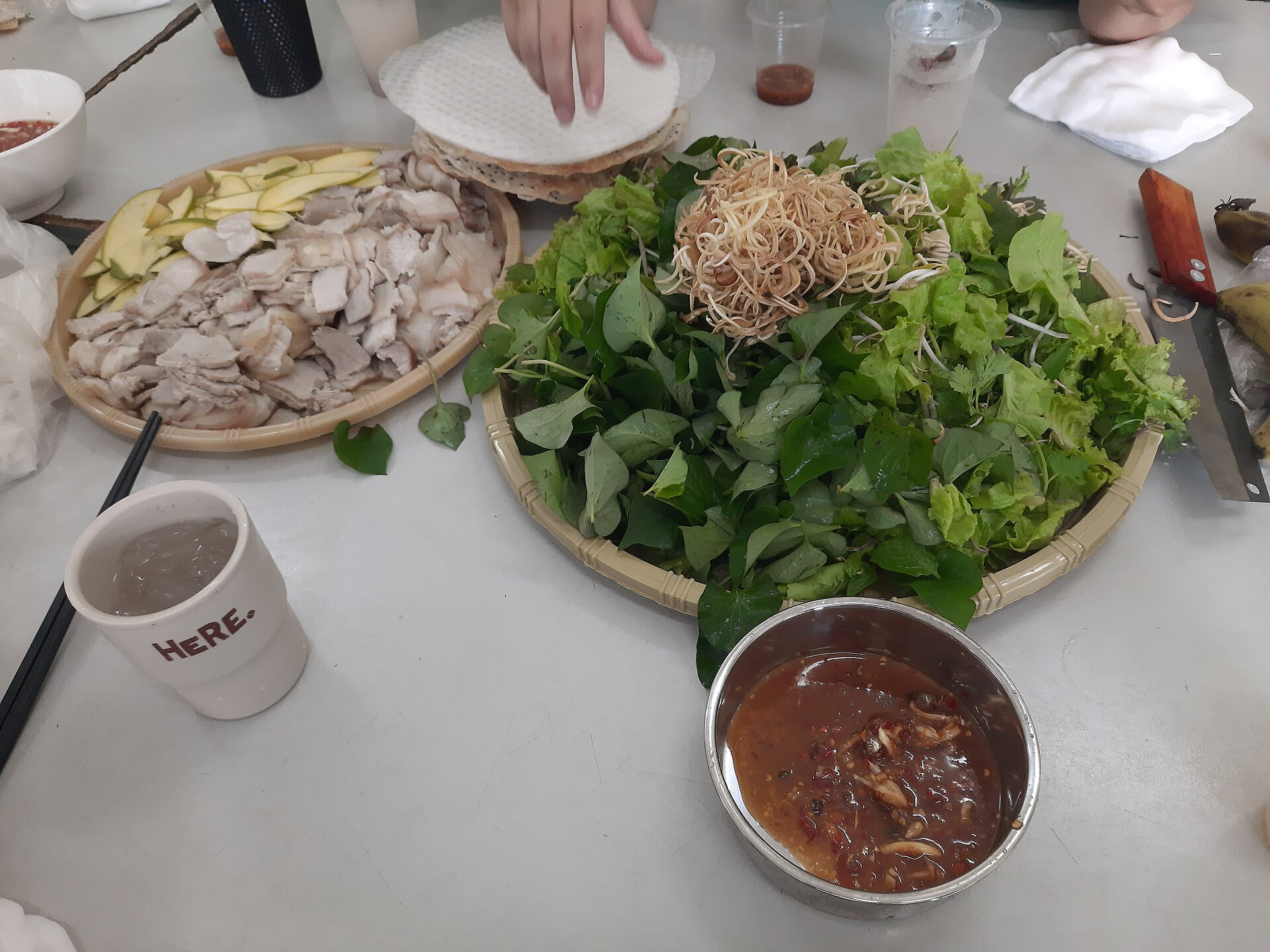 A platter of bánh tráng cuốn thịt heo — sliced boiled pork belly, fresh herbs, rice paper and a bowl of mắm nêm