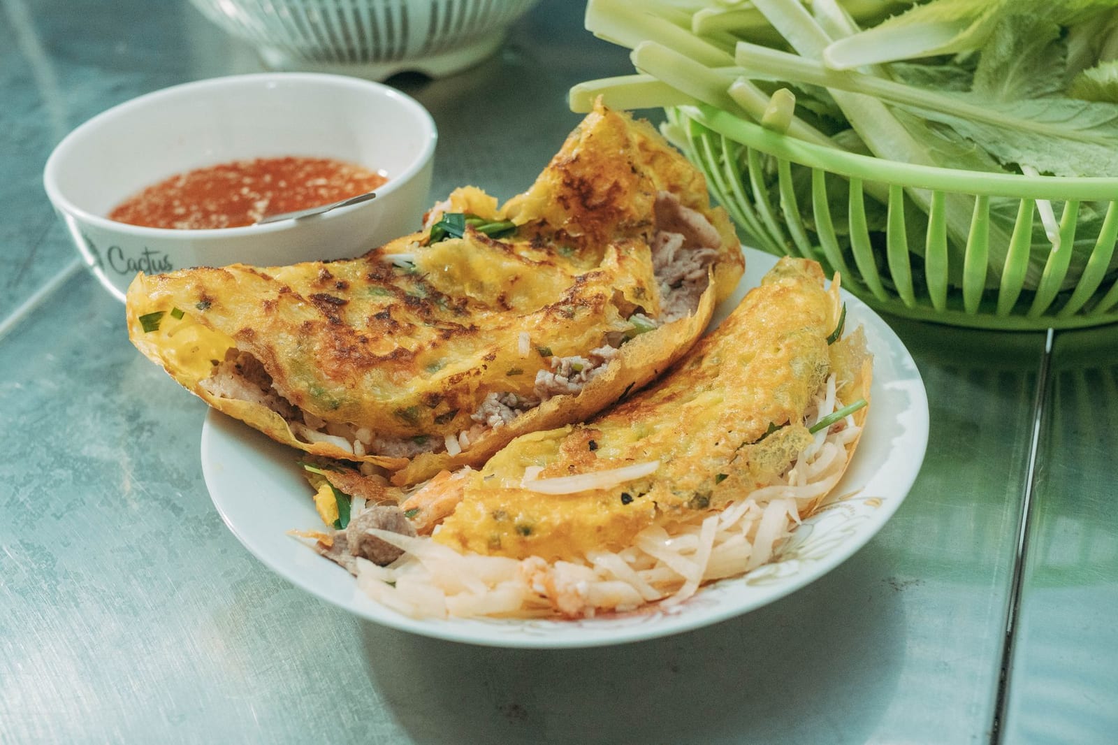 Crispy golden Vietnamese bánh xèo pancakes folded over bean sprouts, plated with fresh herbs and a bowl of dipping sauce