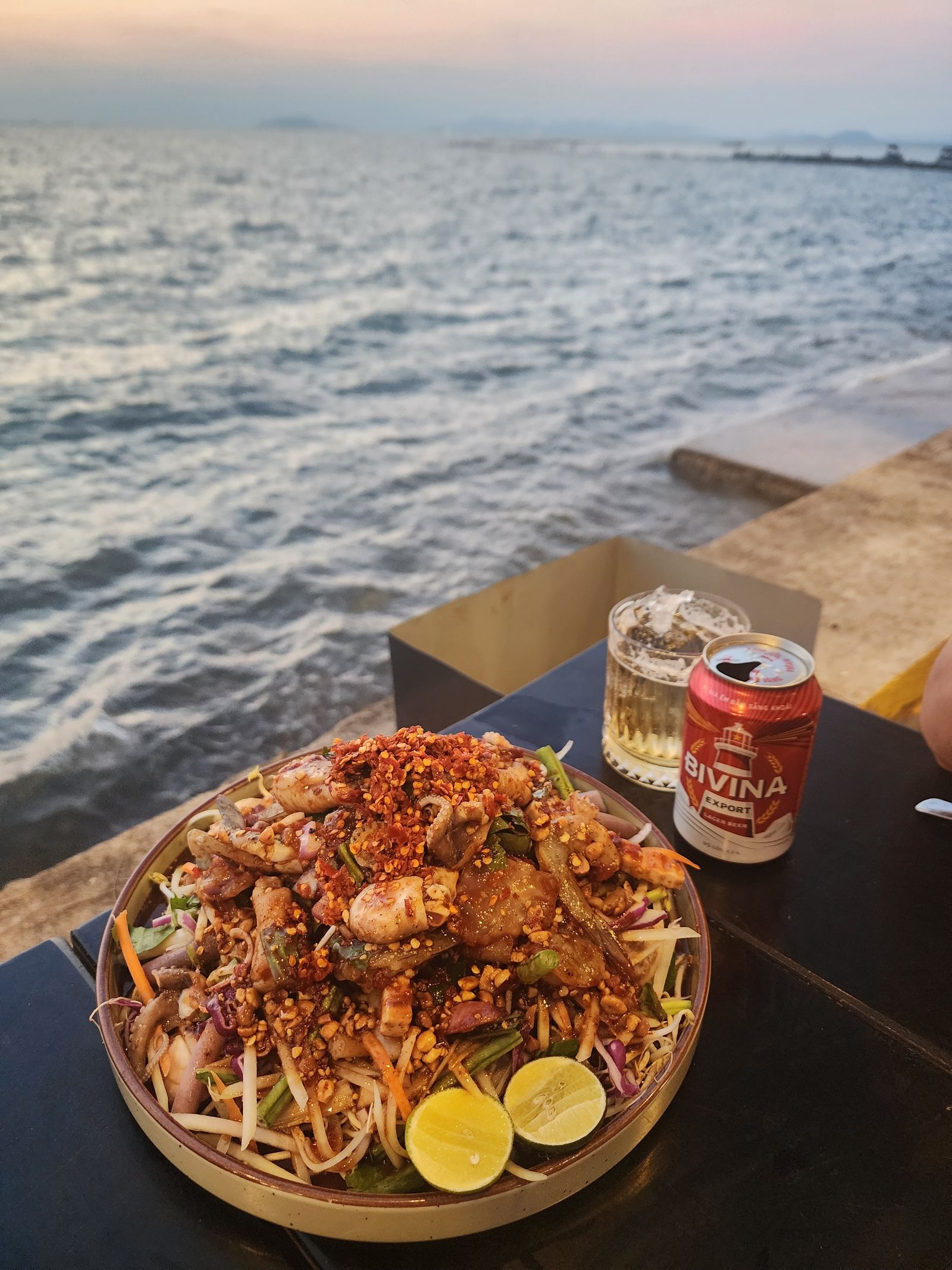 A plate of spicy Vietnamese seafood salad served seaside with a cold drink