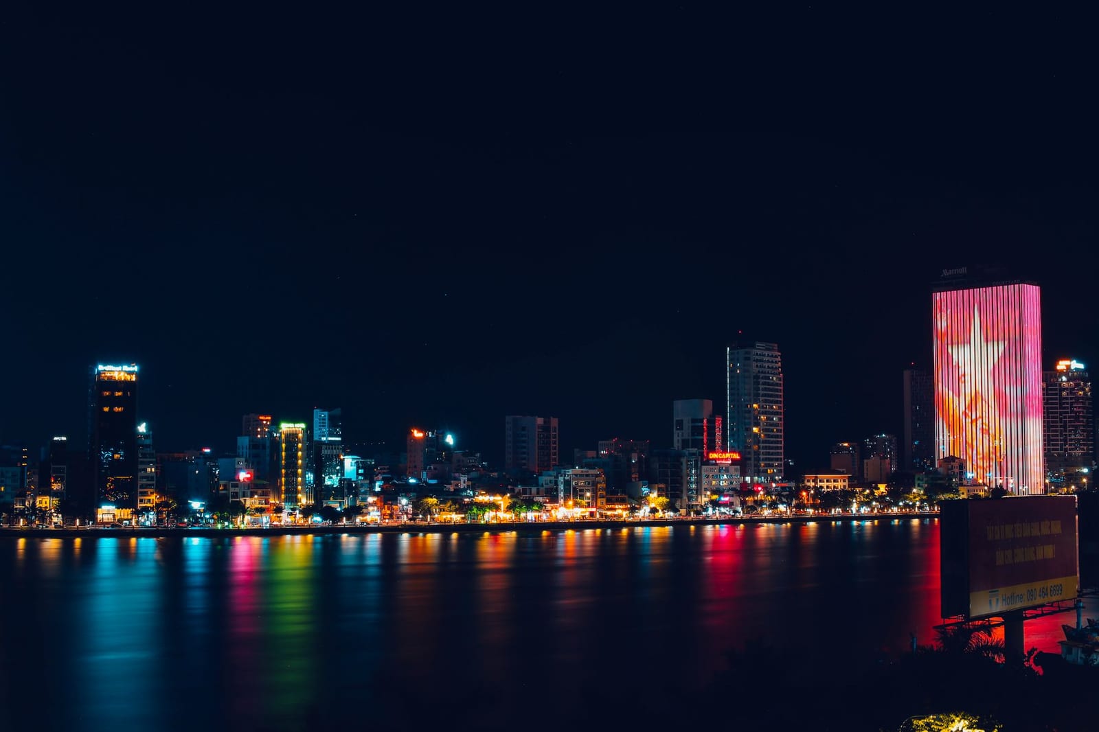 The Da Nang skyline and Bach Dang riverfront lit up at night across the Han River, a popular free fireworks-viewing stretch