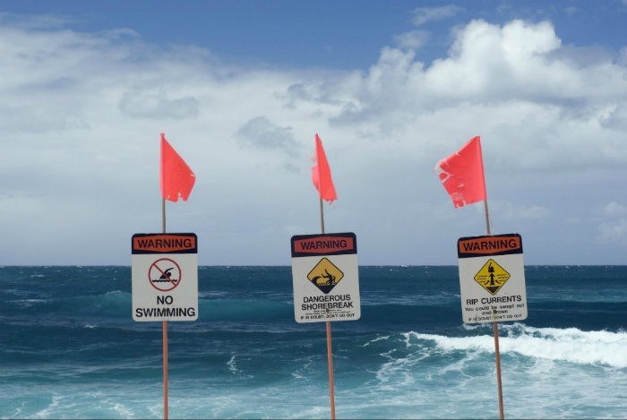 Red warning flags and beach safety signs marking rough surf where swimming is not allowed.