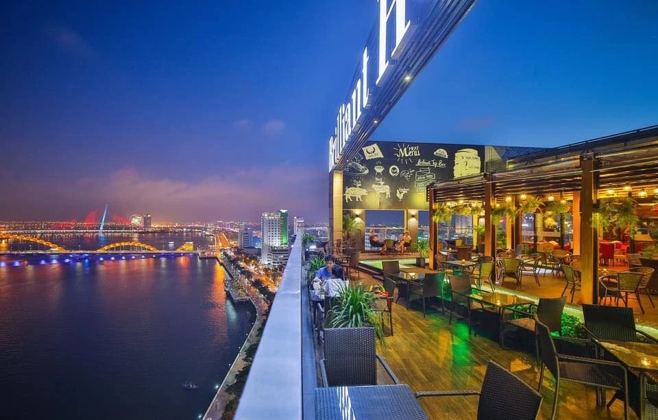 A rooftop bar at night overlooking a river skyline.