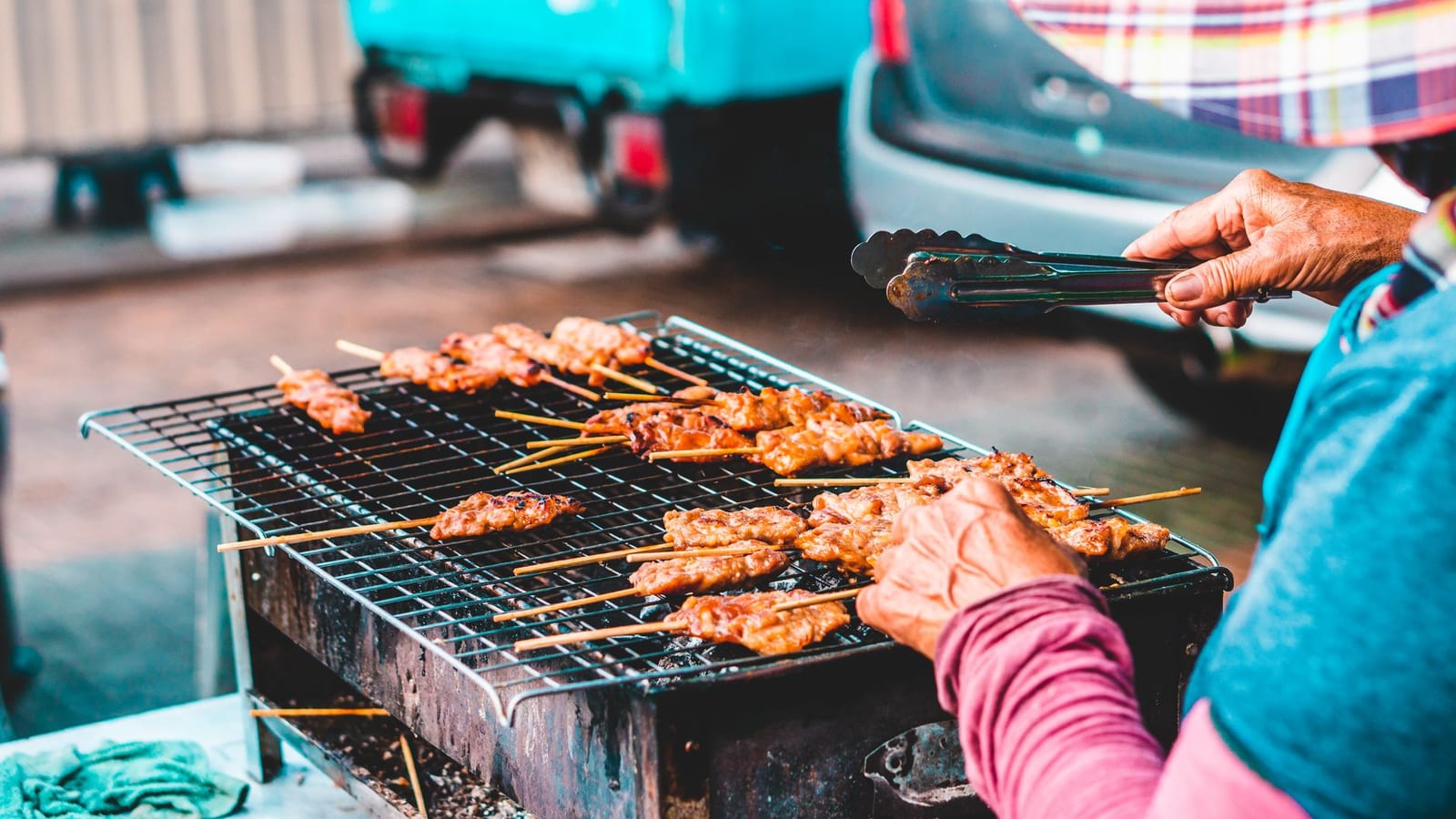A street vendor grilling bamboo skewers over charcoal at a Vietnamese street-food stall.