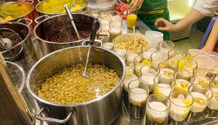 A busy Vietnamese dessert shop with cups of chè lined up on a counter