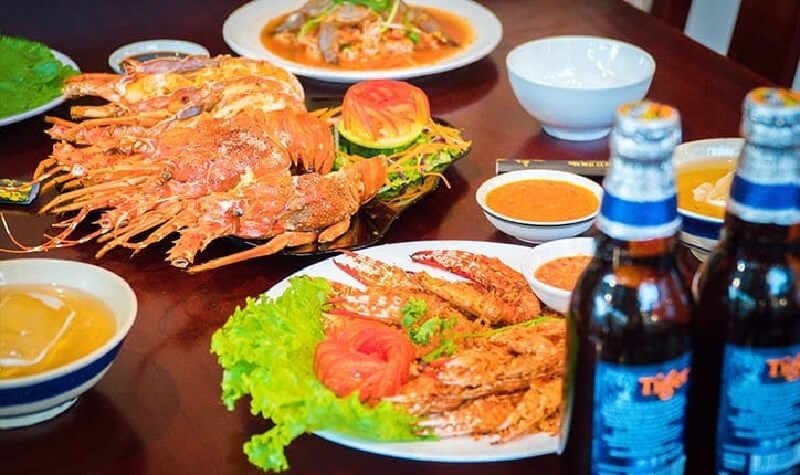A shared nhậu spread of grilled prawns and seafood dishes with bottles of cold beer on the table.