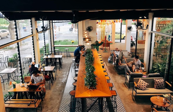 A bright, open-air Da Nang café with a long communal table and ceiling fans where people work on laptops