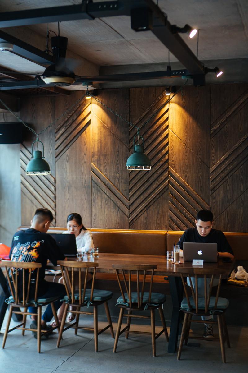 Remote workers on laptops at a wood-panelled specialty café in Da Nang