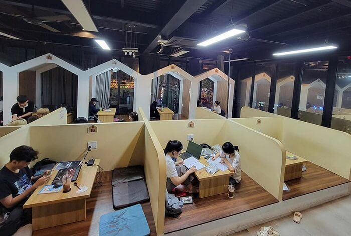 Private wooden study booths at a Da Nang work café, with people typing on laptops over iced coffees