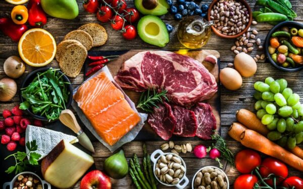 A spread of fresh vegetables, fruit, meat and fish laid out on a wooden table.