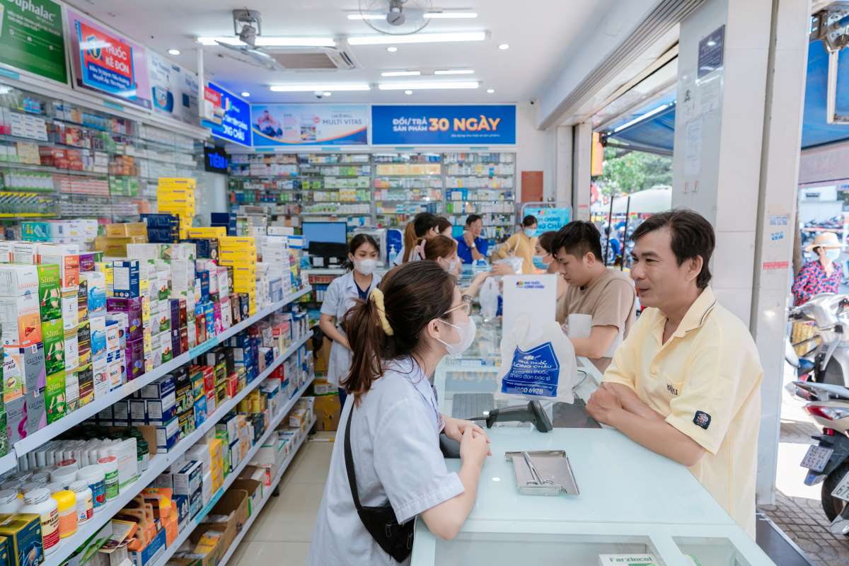 A busy Nhà Thuốc Long Châu branch during opening hours, with uniformed staff serving customers at the counter and a '30-day returns' banner overhead — this is what the chains look like while they are open, and it all shuts by about 10pm