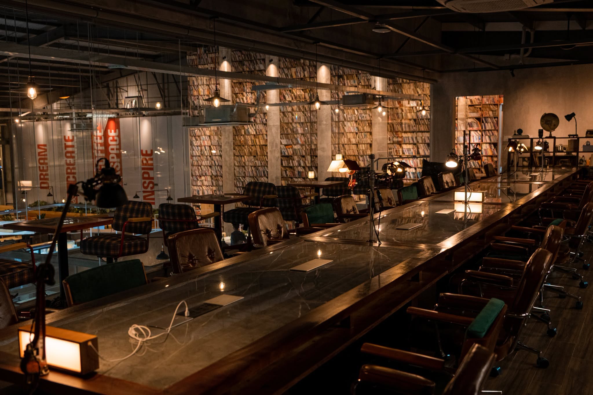 The long shared work counter at HI4 Coffee & Workspace in Da Nang at night, lined with office chairs and task lamps in front of a wall of books.